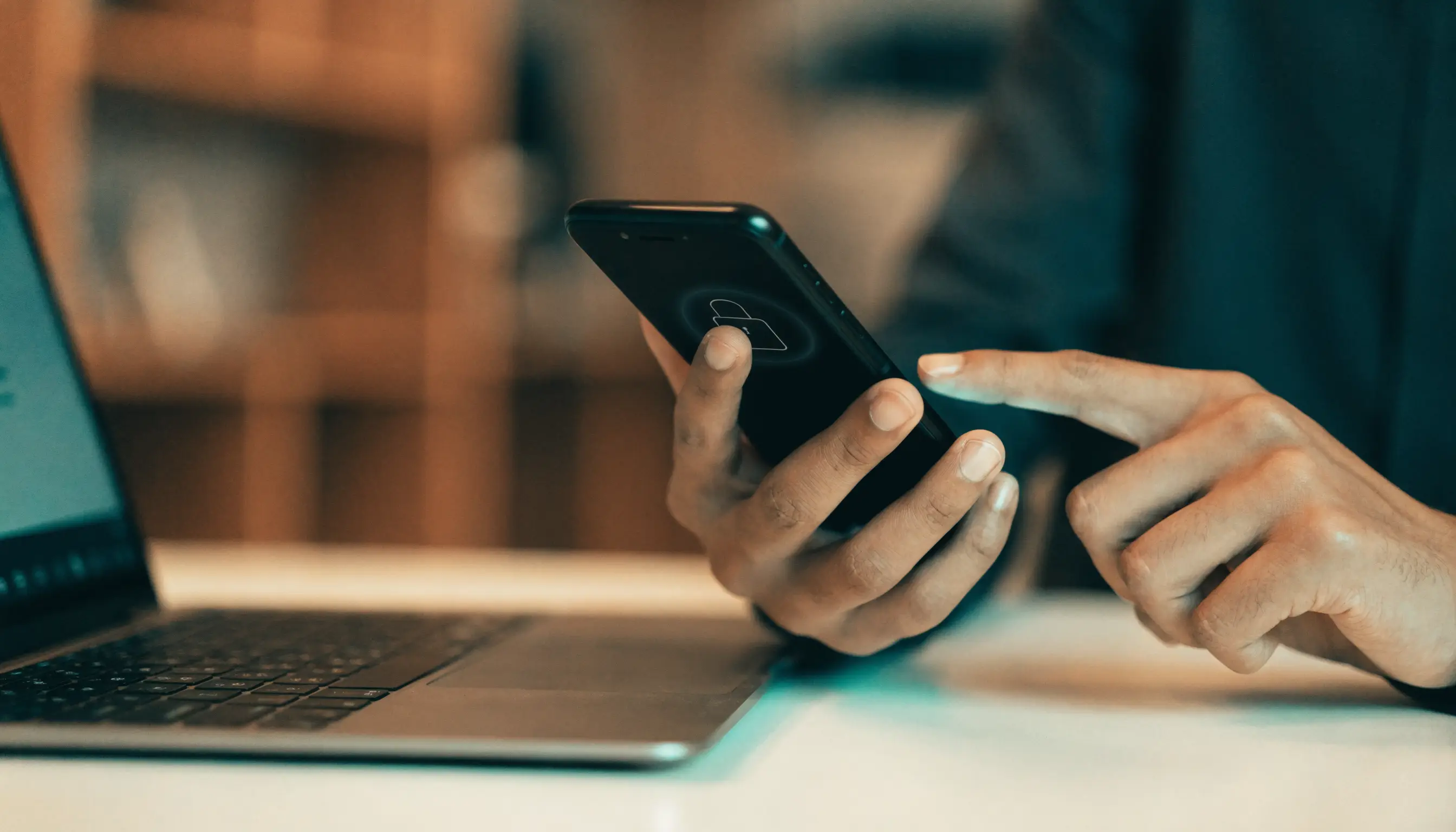 Close-up of hands enabling two-factor authentication on a smartphone next to a laptop in an office.
